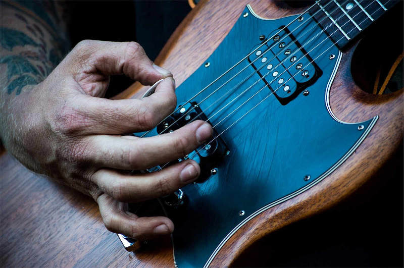 Hand die mit Plektrum Gitarre anschlägt